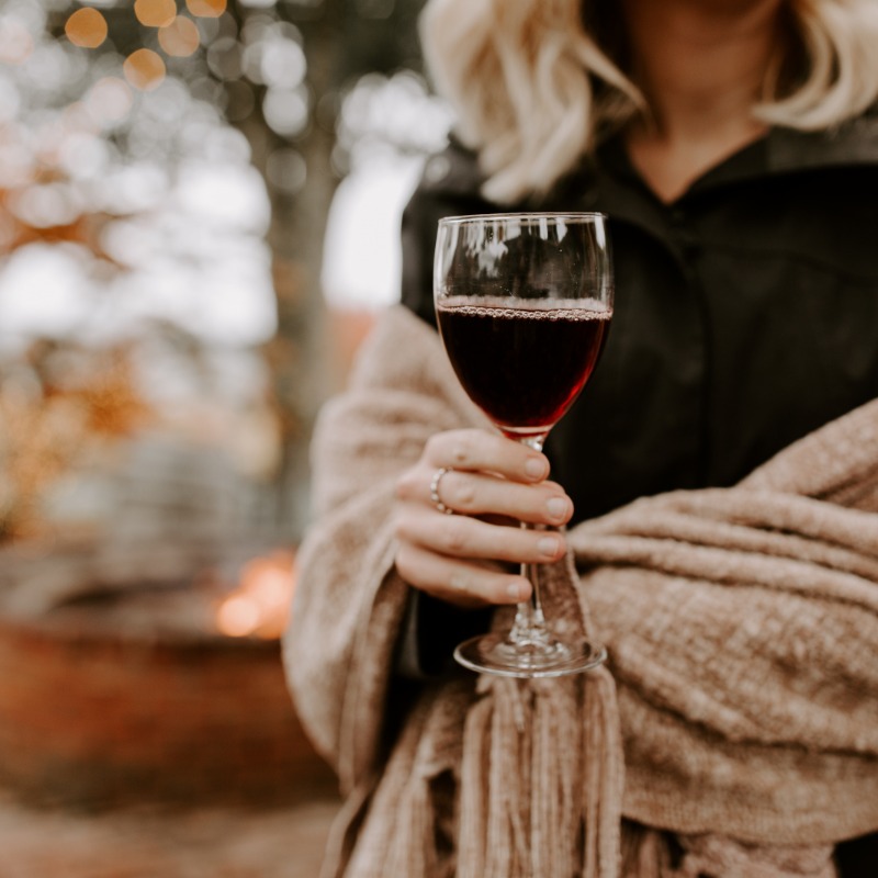 A woman wrapped in a heavy shawl outdoors holds upa glass of Oregon wine